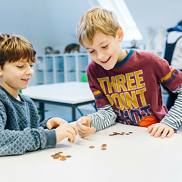 Zwei Jungen sitzen an einem Tisch, auf dem Geldmünzen liegen.