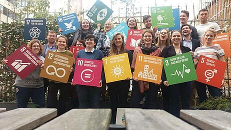Auf dem Bild sieht man viele junge Menschen, die Boxen mit den 17 Zielen für eine nachhaltige Entwicklung in der Hand halten