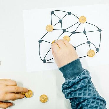 Hände setzen braune Steine auf ein Bild, auf dem ein Netzwerk abgebildet ist.