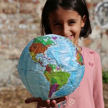 Ein Mädchen hält einen aufblasbaren Globus in die Kamera.