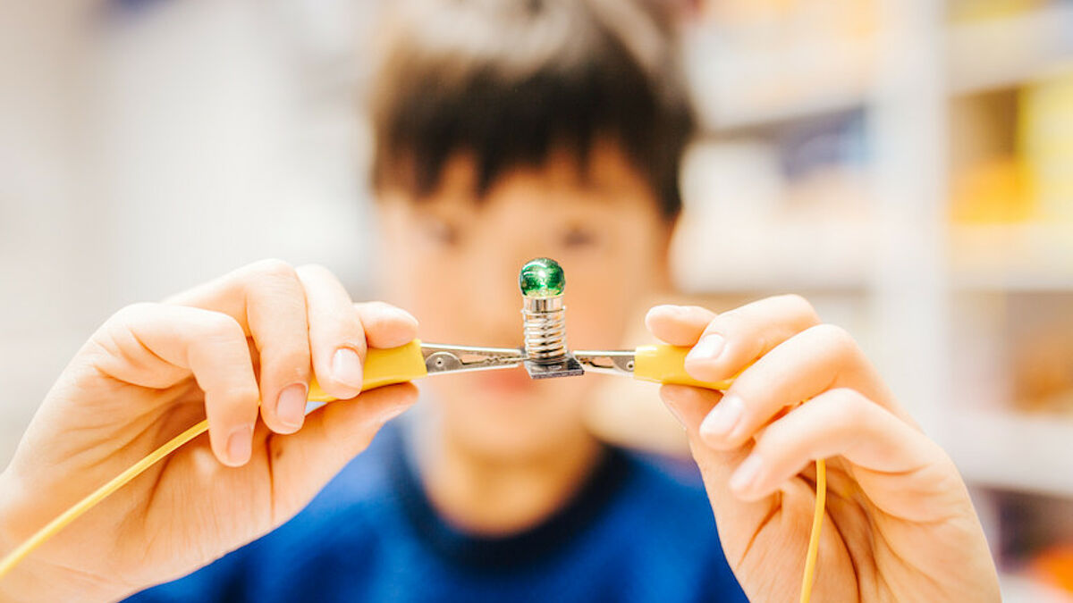 Kind erzeugt einen Stromkreis mit zwei Kabeln und einer kleinen Lampe