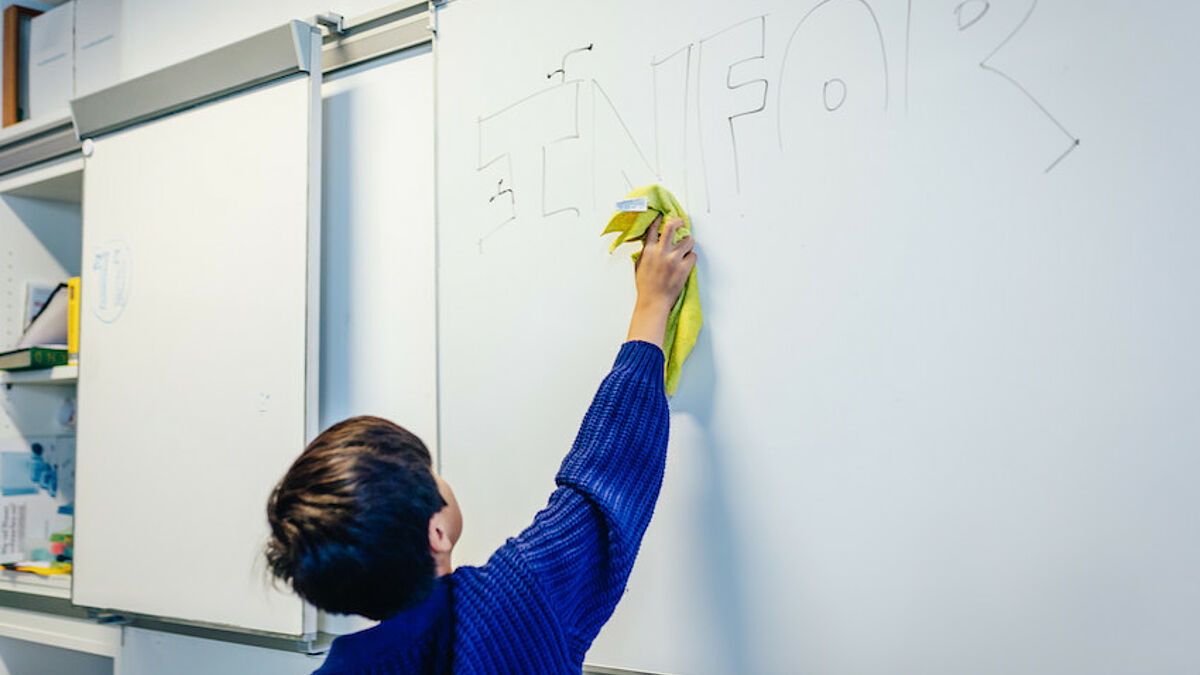 Kind wischt einen Schriftzug von einer weißen Tafel