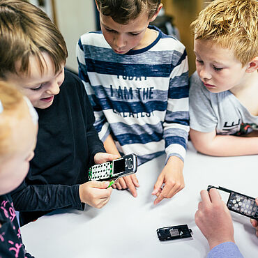 Kinder zerlegen ein altes Handy in Einzelteile