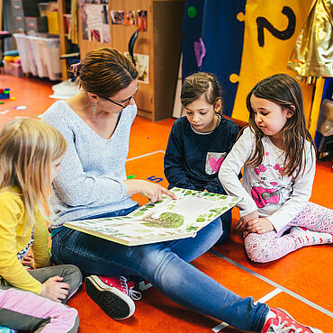 Eine Erzieherin schaut sich gemeinsam mit Kindern ein Buch an