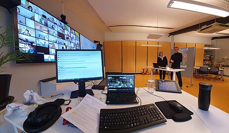 Ein weiter Blick in einen Seminarraum, ein Mann und eine Frau stehen vor einem großen Bildschirm