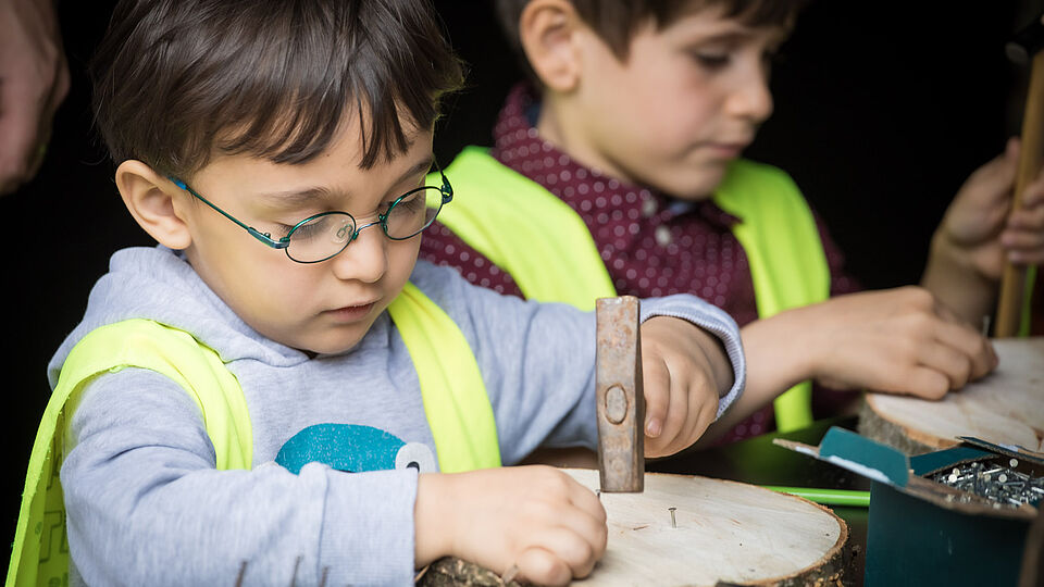 Zwei Jungen hämmern Nägel in Holzscheiben