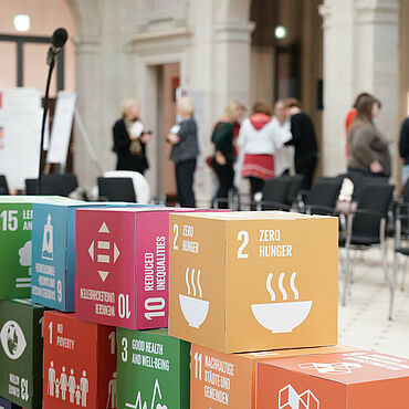 Bunte Würfel mit den internationalen Nachhaltigkeitszielen stehen gestapelt auf einer Veranstaltung